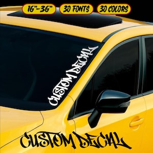 May include: Yellow car with a black windshield decal that says "CUSTOM DECAL" in a stylized font. The decal is white. The image also shows text that says "16"-36" 30 FONTS 30 COLORS" in a yellow and black banner.