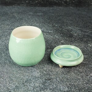 May include: A green ceramic jar with a lid. The jar has a textured surface and the lid has a swirl design.