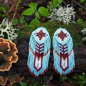 Könnte beinhalten: Ein Paar türkisblaue Perlenohrringe mit geometrischem Muster und Fransen. Die Ohrringe sind aus weißen, braunen und roten Perlen gefertigt.