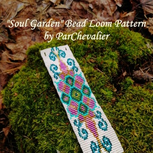 Könnte beinhalten: Weißes Perlenarmband, das auf einem Webstuhl gewebt wurde, mit einem farbenfrohen Blumendesign aus türkisfarbenen, rosafarbenen und goldenen Perlen. Das Armband trägt den Titel "Soul Garden" Bead Loom Pattern by ParChevalier.