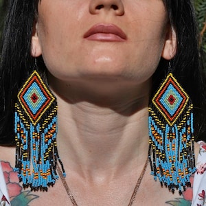 May include: A pair of long, beaded earrings with a geometric diamond pattern in shades of blue, yellow, red, and black.