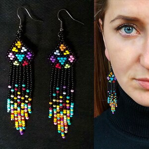 Könnte beinhalten: Ein Paar lange, bunte Perlenohrringe mit geometrischem Design. Die Ohrringe sind aus schwarzen Perlen gefertigt und haben eine Vielzahl von Farben, darunter Pink, Blau, Gelb und Grün.