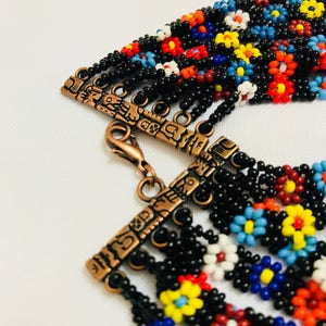 May include: A beaded necklace with a multi-colored floral pattern. The necklace has a copper clasp with an intricate design.
