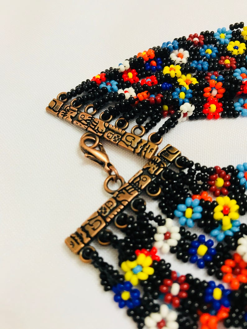 May include: A beaded necklace with a multi-colored floral pattern. The necklace has a copper clasp with an intricate design.