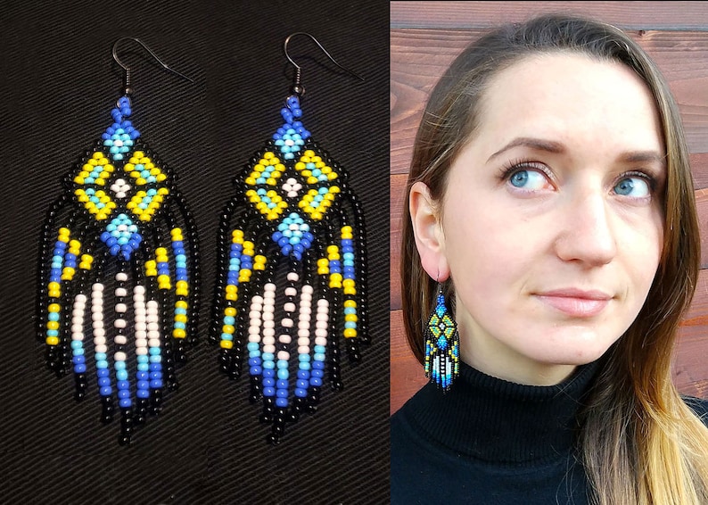 May include: A pair of long, beaded earrings with a geometric pattern in black, white, blue, and yellow. The earrings are hanging from a woman's earlobes.