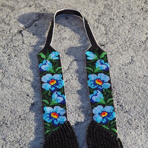以下が含まれることがあります： 青と緑の花柄が施された黒いビーズのストラップ2本。ストラップの下部には黒いタッセルが付いている。