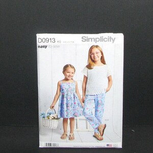 May include: Simplicity sewing pattern D0913 for girls' clothing. The pattern cover shows two girls wearing a floral print dress and matching trousers and top. The words "easy to sew" are printed on the cover.