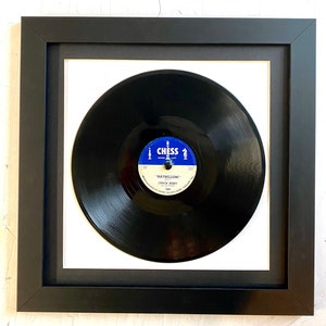 May include: A black vinyl record in a black frame with a white mat. The record label is blue and white and says "Chess" and "Maybellene" by "Chuck Berry".