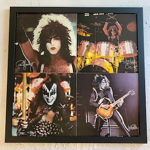 May include: A framed collage of four photographs featuring the rock band KISS. Each quadrant displays a band member in stage makeup and costume, including Paul Stanley, Peter Criss, Gene Simmons, and Ace Frehley, with their respective signatures.