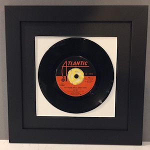 May include: A black vinyl record with a yellow label. The label says "Atlantic" and "You Shook Me All Night Long" by AC/DC. The record is framed in a black frame with a white mat.