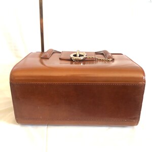 May include: A brown leather handbag with a gold chain and a silver clasp. The bag has a smooth, glossy finish and is closed with a flap.