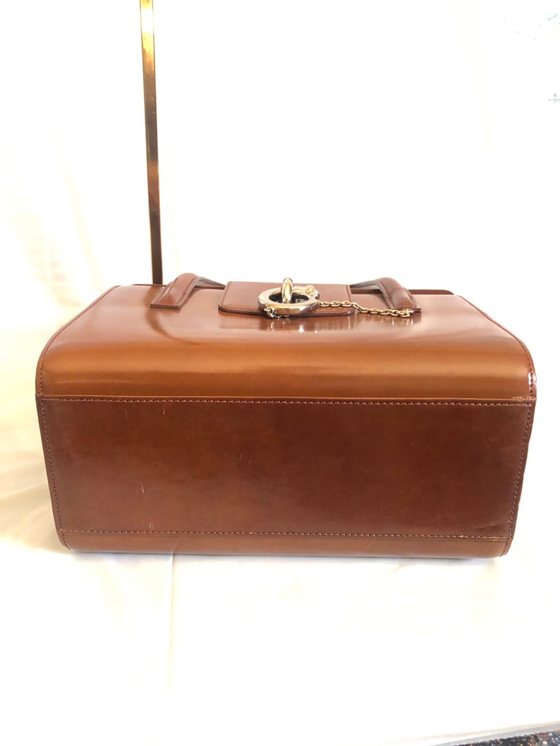 May include: A brown leather handbag with a gold chain and a silver clasp. The bag has a smooth, glossy finish and is closed with a flap.