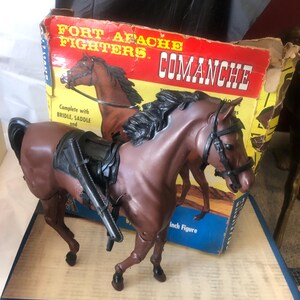 Peut inclure: Un cheval en plastique marron nommé Comanche de la ligne de jouets Fort Apache Fighters. Le cheval porte une selle et une bride noires. La boîte est jaune avec des accents rouges et bleus.