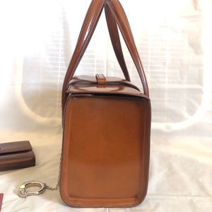 May include: A brown leather handbag with a top handle and a chain strap. The bag is closed and has a shiny finish.