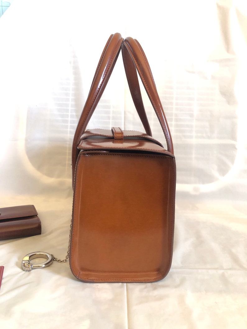 May include: A brown leather handbag with a top handle and a chain strap. The bag is closed and has a shiny finish.