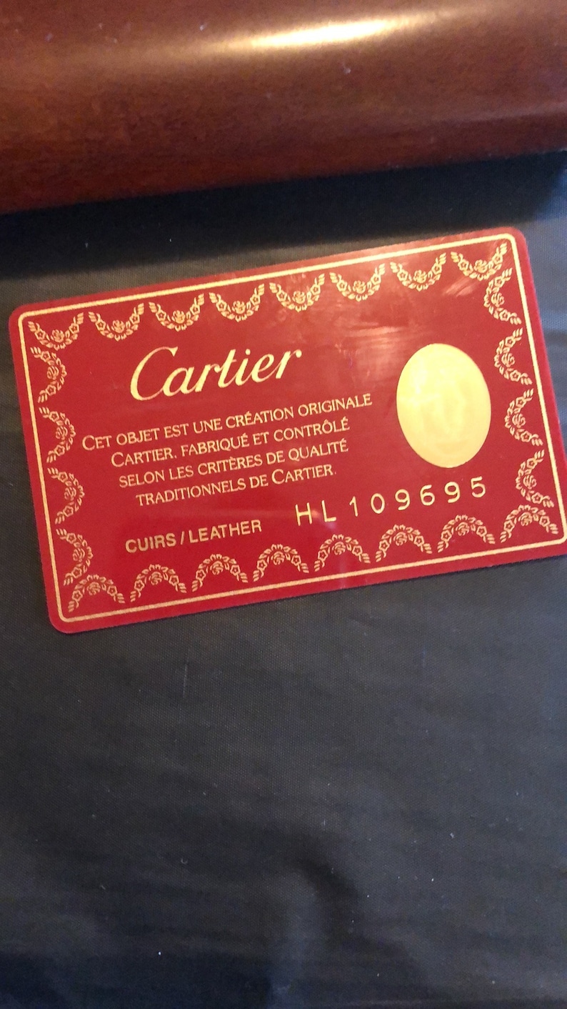 May include: A red Cartier authenticity card with gold lettering. The card reads 'CET OBJET EST UNE CRÉATION ORIGINALE CARTIER. FABRIQUÉ ET CONTRÔLÉ SELON LES CRITÈRES DE QUALITÉ TRADITIONNELS DE CARTIER.'  CUIRS/LEATHER HL 109695
