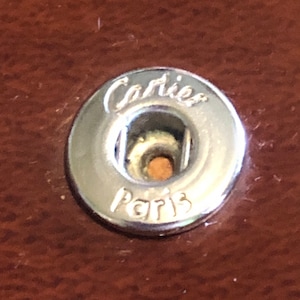 May include: A silver metal button with the words 'Cartier Paris' engraved on it.