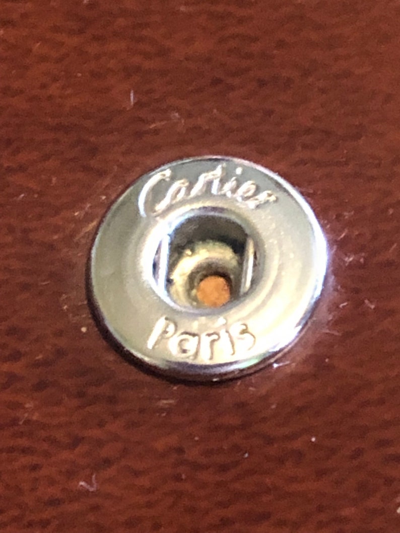 May include: A silver metal button with the words 'Cartier Paris' engraved on it.