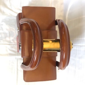 May include: A brown leather handbag with gold hardware. The bag has two top handles and a buckle closure.