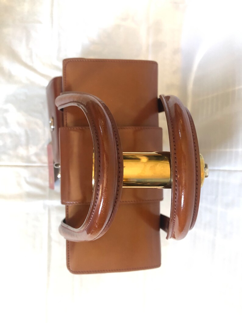 May include: A brown leather handbag with gold hardware. The bag has two top handles and a buckle closure.