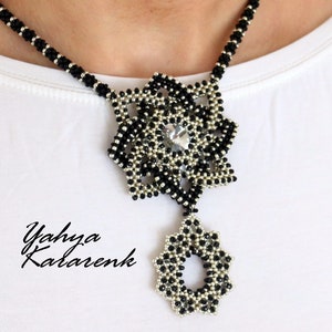 May include: A black and silver beaded necklace with a large, intricate pendant featuring a crystal in the centre. The pendant is shaped like a flower with multiple layers of beads.