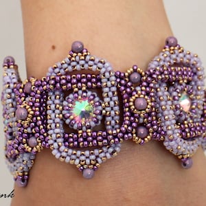 Op de afbeelding: Een paarse en gouden kralen armband met een geometrisch ontwerp en iriserende kristallen.