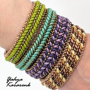 May include: A stack of colorful beaded bracelets in shades of green, turquoise, purple, gold, and cream. The bracelets are made with small seed beads and feature a herringbone stitch pattern.