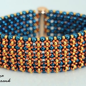 Könnte beinhalten: Ein Perlenarmband mit einem sich wiederholenden Blumenmuster. Das Armband besteht aus blauen, goldenen und kupferfarbenen Perlen. Der Verschluss ist goldfarben. Das Armband ist etwa 3,8 cm breit.