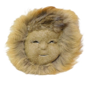 May include: A plush doll head with a smiling face and a fur-like mane. The doll's face is a light tan color, with stitched eyes and a small, curved mouth. The surrounding fur is a mix of brown and tan.