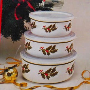 May include: A stack of three white ceramic bowls with clear lids. Each bowl is decorated with a repeating pattern of brown holly leaves and red berries. The bowls are a festive holiday theme.