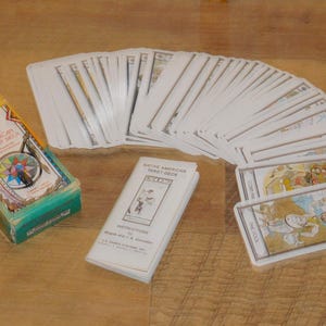 May include: A Native American Tarot Deck with a box, instruction booklet, and fanned-out cards. The box is yellow, green, and orange with a compass design. The cards feature illustrations with Native American themes.