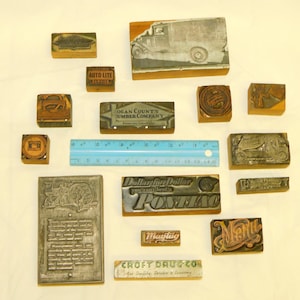 May include: A collection of vintage wood and metal printing blocks. The blocks feature various logos and text, including "Auto-Lite Service", "Ogan County Umber Company", "Dollar for Dollar You Can't Beat It Pontiac", "Maytag", and "Croft Drug Co.".