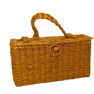 May include: A rectangular, woven basket with a braided handle and a lid. The basket is a warm, golden brown color and features a circular clasp. The handle is arched, and the basket appears to be made of natural fibers.