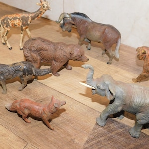 May include: A collection of vintage animal figurines, including a giraffe, bear, wolf, fox, elephant, wildebeest, and tiger. The figurines are painted in various colors and appear to be made of a durable material.