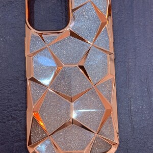 May include: A rose gold phone case with a geometric design and a glittery finish.