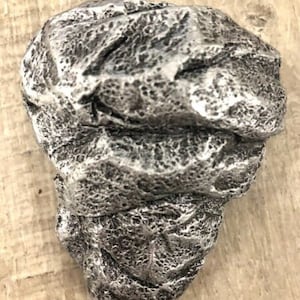May include: A silver-coloured, textured rock-shaped object with a rough, uneven surface. The object is made of a material that resembles stone.