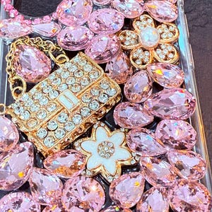 May include: A clear phone case decorated with pink and gold rhinestones, including a small purse-shaped rhinestone design.