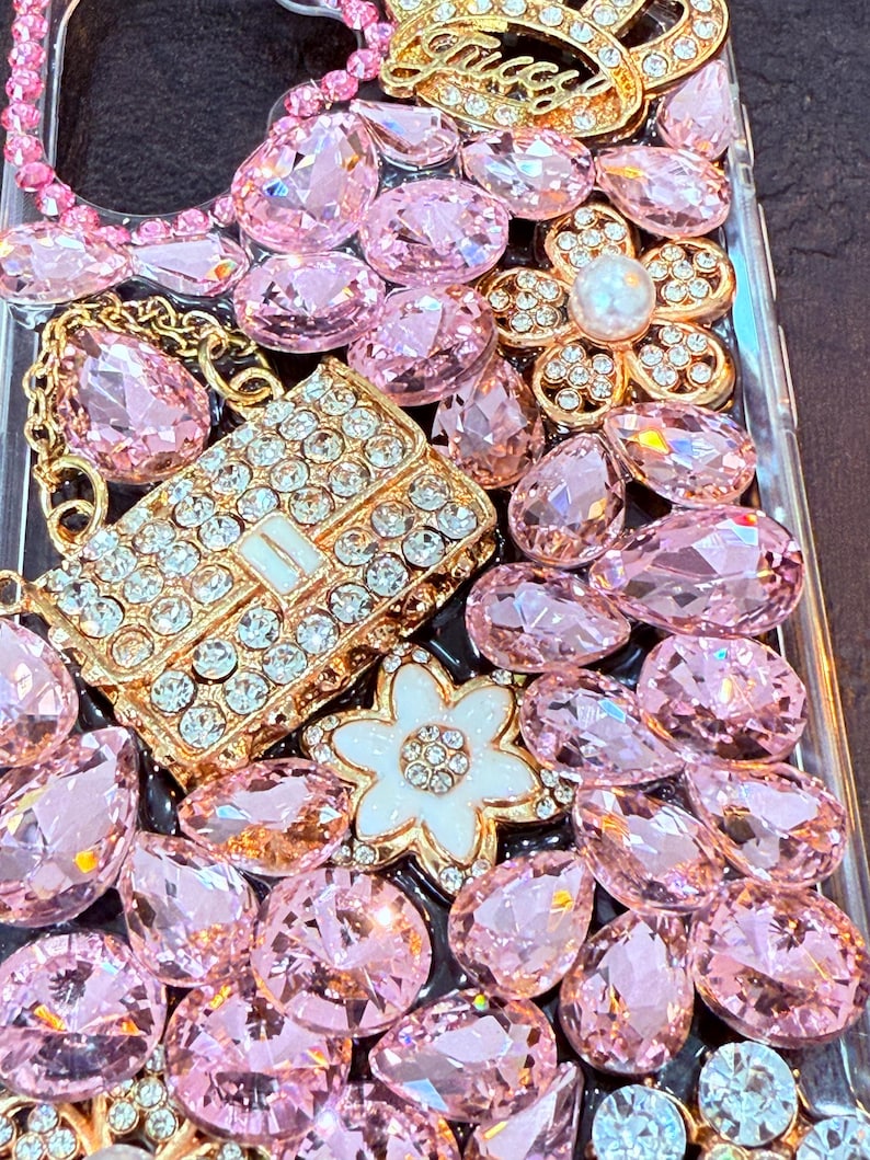 May include: A clear phone case decorated with pink and gold rhinestones, including a small purse-shaped rhinestone design.