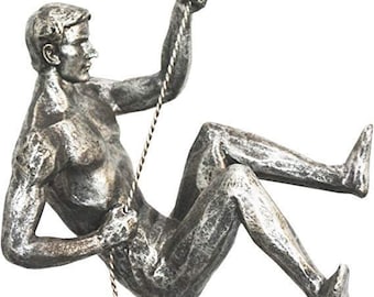 Figura de hombre escalando en rappel, de color plata antigua, con el brazo izquierdo hacia arriba, colgando de un alambre, para colgar en la pared.