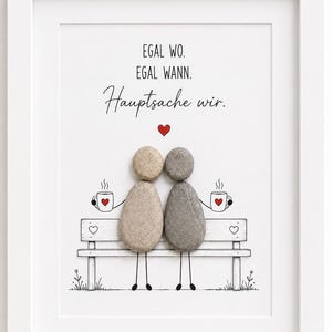 Könnte beinhalten: Ein gerahmtes Kieselsteinbild mit zwei Figuren aus glatten Steinen, die auf einer gezeichneten Bank sitzen und Tassen mit roten Herzen halten. Der Text lautet: EGAL WO. EGAL WANN. Hauptsache wir. Ein kleines rotes Herz befindet sich über den Figuren.