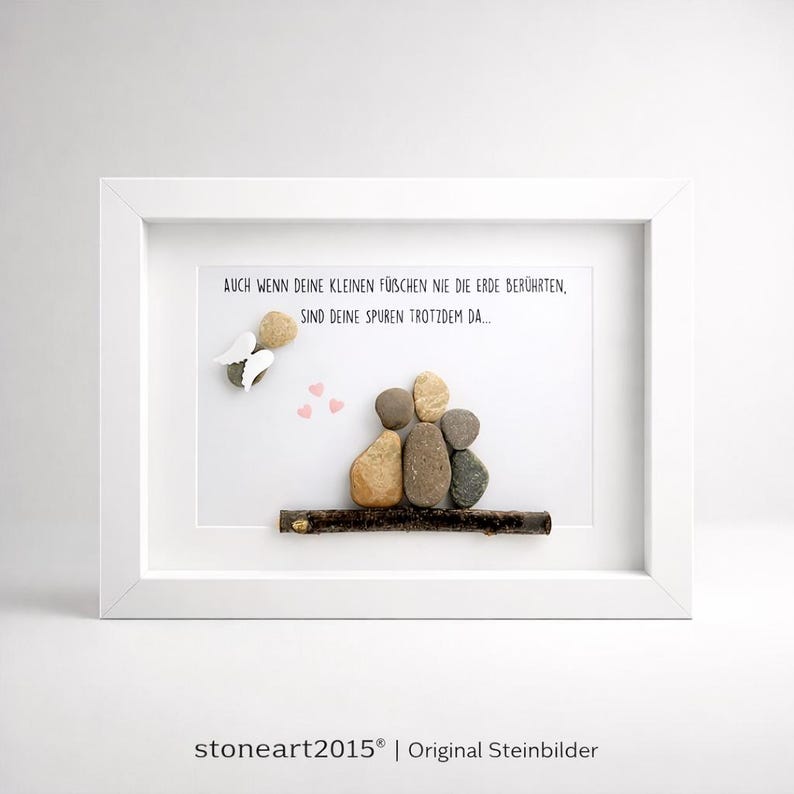 May include: A framed artwork featuring a family of four depicted with smooth stones on a wooden branch. Above, an angel made of stones and three pink hearts are displayed. The text reads, "AUCH WENN DEINE KLEINEN F&Uuml;BCHEN NIE DIE ERDE BER&Uuml;HRTEN, SIND DEINE SPUREN TROTZDEM DA..."
