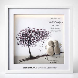 Può includere: Un'opera d'arte incorniciata con un albero con foglie a forma di cuore in tonalità viola. Due figure di ciottoli sedute sotto, con calici di champagne. Il testo in tedesco recita "Alles Liebe zur Rubinhochzeit". Firmato "stoneart2015".
