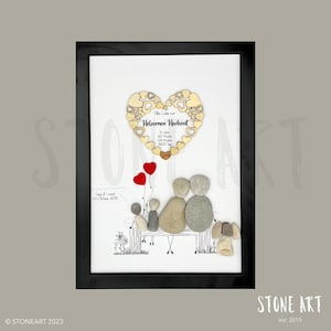 May include: Framed artwork featuring a family depicted with stones on a bench, with red heart balloons. A wooden heart with text in German is at the top. The artwork is in a black frame.