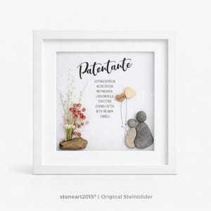 Könnte beinhalten: Ein quadratischer weißer Rahmen mit einem Wandbild, das den deutschen Text Patentante, Vertrauensperson, Bezugsperson, Mutmacherin, Lebensmensch, Schutzende, Liebende Patin, Beste Freundin, Vorbild, Trockenblumen und Kieselsteinfiguren zeigt.