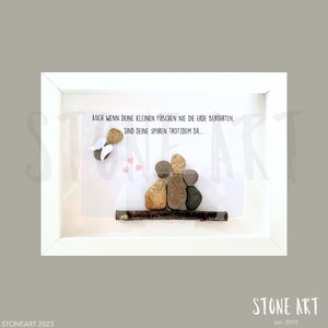 May include: A framed artwork featuring a family of four depicted with smooth stones on a white background. An angel made of stones and wings is on the left. The text reads "AUCH WENN DEINE KLEINEN F&Uuml;BCHEN NIE DIE ERDE BER&Uuml;HRTEN, SIND DEINE SPUREN TROTZDEM DA..."