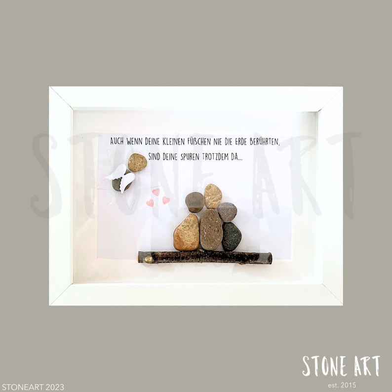 May include: A framed artwork featuring a family of four depicted with smooth stones on a white background. An angel made of stones and wings is on the left. The text reads "AUCH WENN DEINE KLEINEN F&Uuml;BCHEN NIE DIE ERDE BER&Uuml;HRTEN, SIND DEINE SPUREN TROTZDEM DA..."