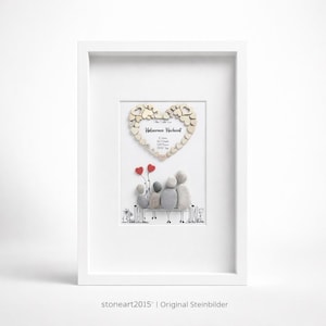 May include: Framed artwork featuring a family of stone figures seated on a bench, with red heart balloons. A wooden heart with text is above the family. The artwork is in a white frame.