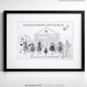 Könnte beinhalten: Ein gerahmtes Wandbild mit Steinfiguren, die medizinisches Personal und ein Kind vor einem gezeichneten Krankenhaus und Krankenwagen darstellen. Der Text lautet: Kleine Menschen brauchen so große Herzen wie eure. Danke für alles! Elias ruft mit Mama und Papa.