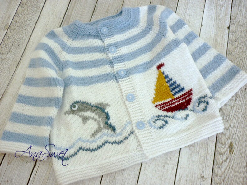 May include: A white and blue striped knitted baby cardigan with a dolphin and sailboat design. The cardigan has a button closure and is made of soft yarn.