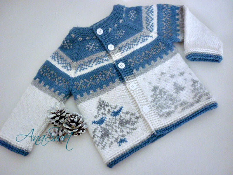 May include: A blue and white knitted baby cardigan with a snowflake and tree pattern. The cardigan has a button closure and is made with a soft yarn.